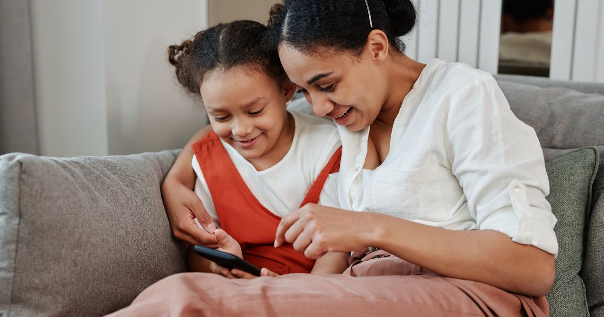 A mother and daughter on the couch, buying tickets together on a phone