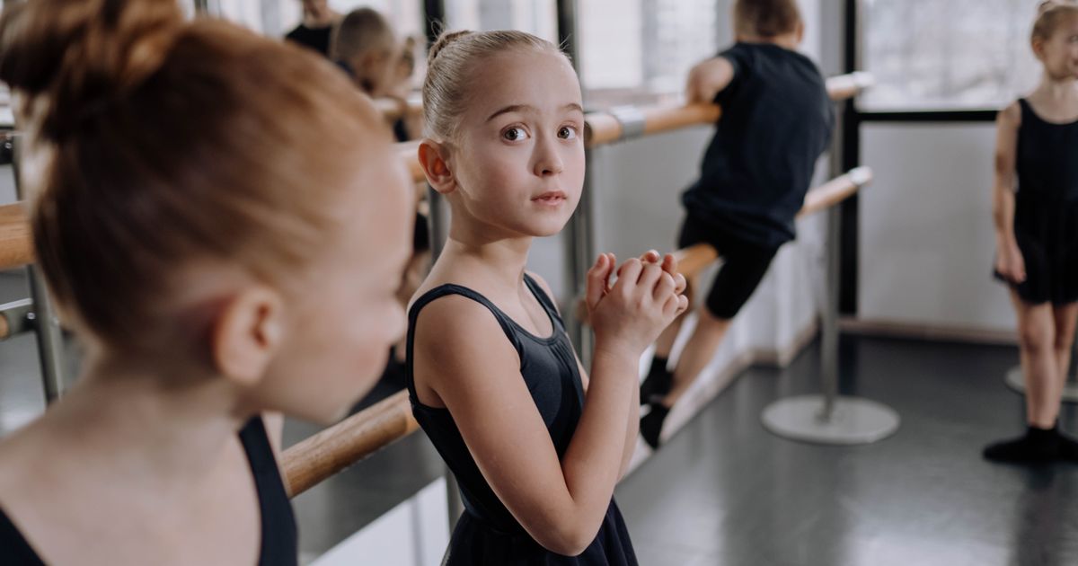 A young dancer at the barre glancing toward the side of the studio