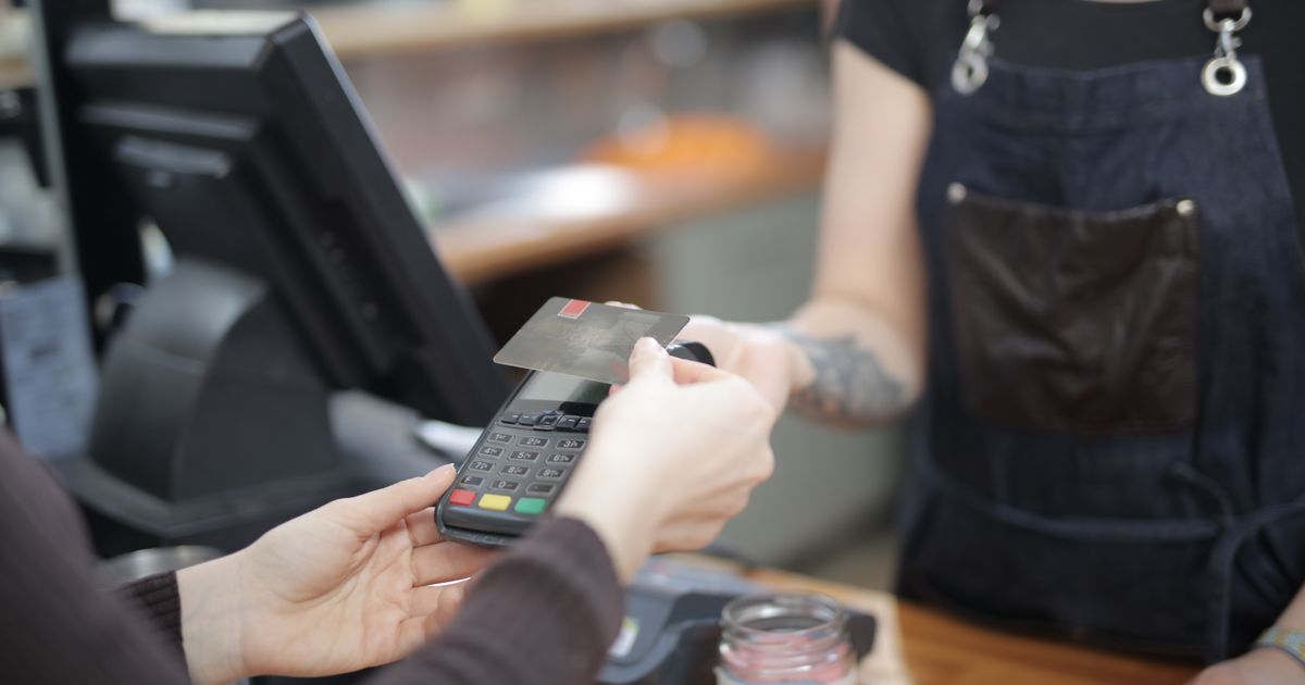 A customer paying by card at a shop counter, the cashier holding the terminal
