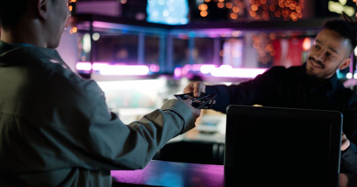 A smiling man handing a pair of tickets across the box office counter
