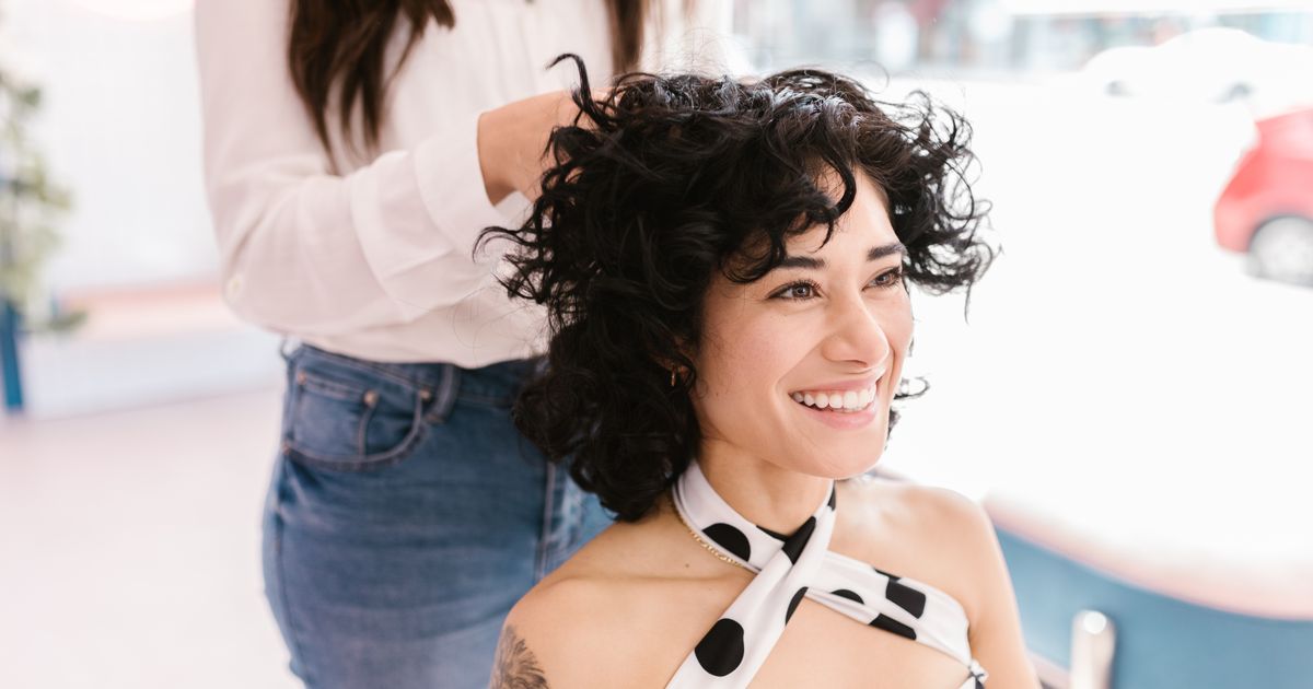 A client with curly hair smiling as the stylist finishes the cut