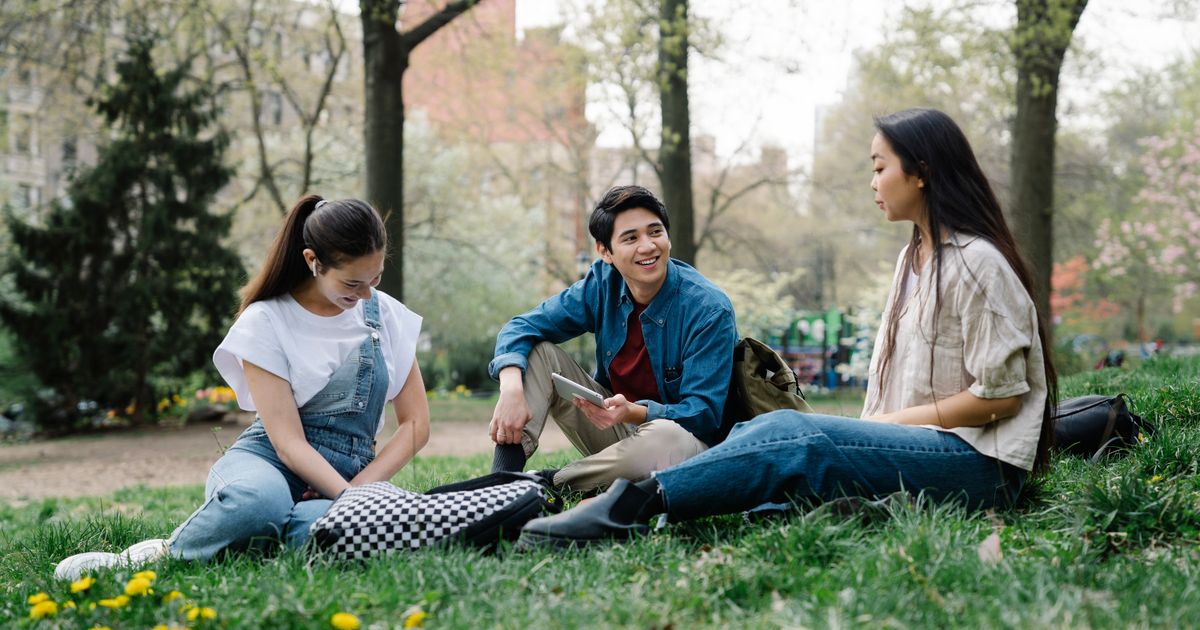 A group of young adults sitting on the grass in a park, talking together