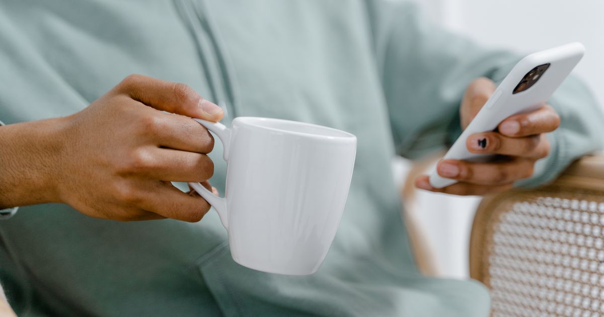 Hands holding a morning coffee and a phone, where the offer of a spot arrives
