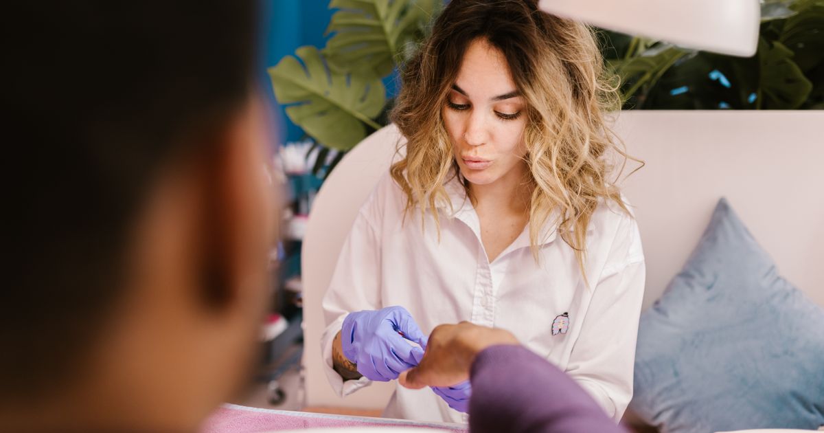 A nail technician working on a client's manicure, hands too busy for the phone
