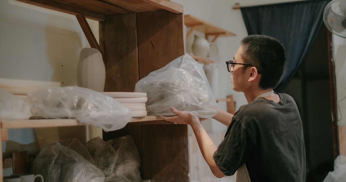 A potter shelving pieces wrapped in plastic to dry slowly before firing