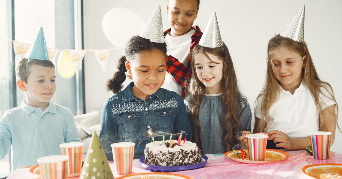 Children in party hats gathered around a birthday cake at the party table