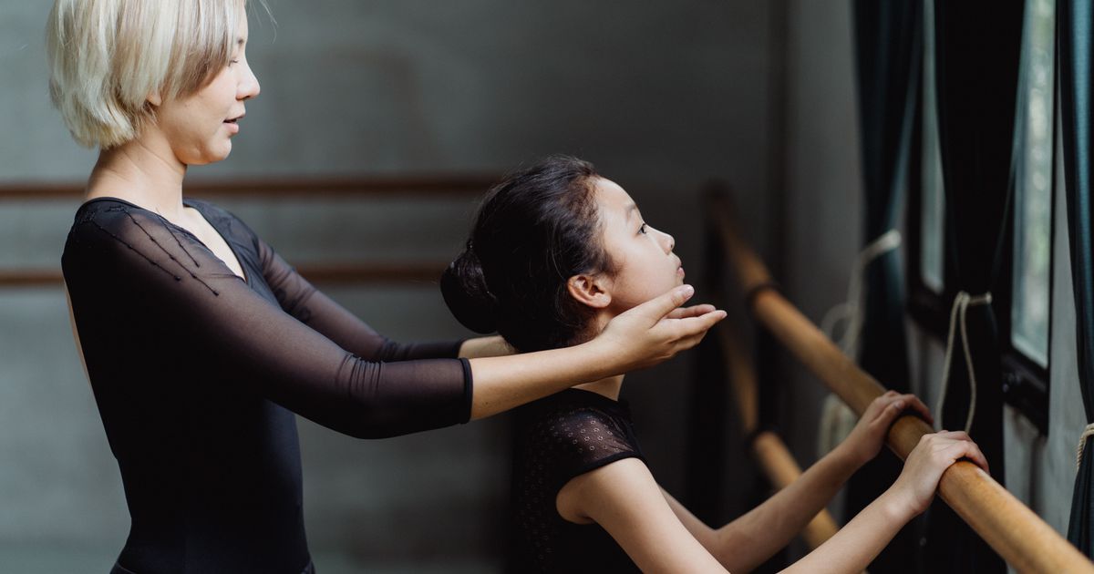 A dance teacher working one-on-one with a student at the barre