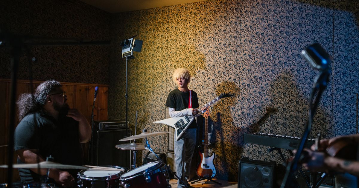 A young guitarist and a drummer rehearsing in a small room with amps and a keyboard