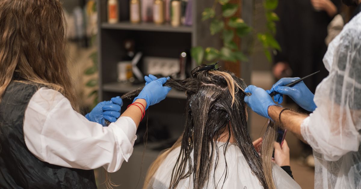 Two stylists working on one client in a busy salon