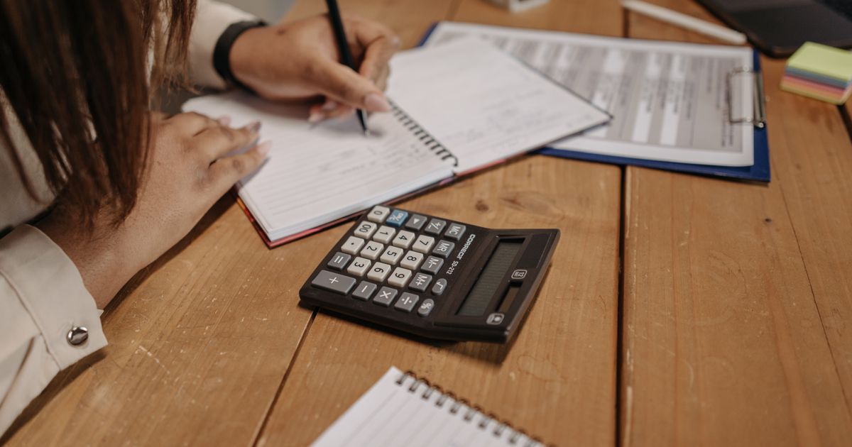 An owner writing a few numbers in a notebook at a wooden desk, with a calculator beside it