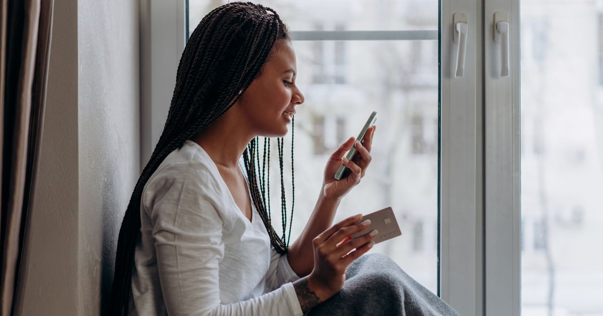 A woman by the window, paying for tickets on a phone, card in hand