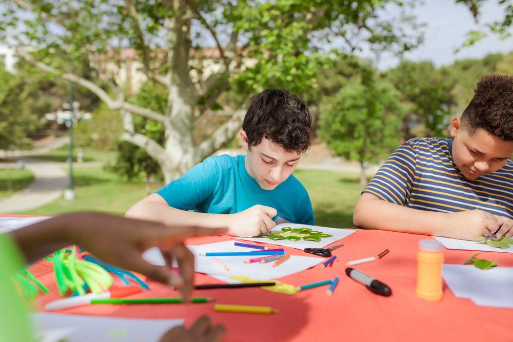 Campers drawing at a table under the trees