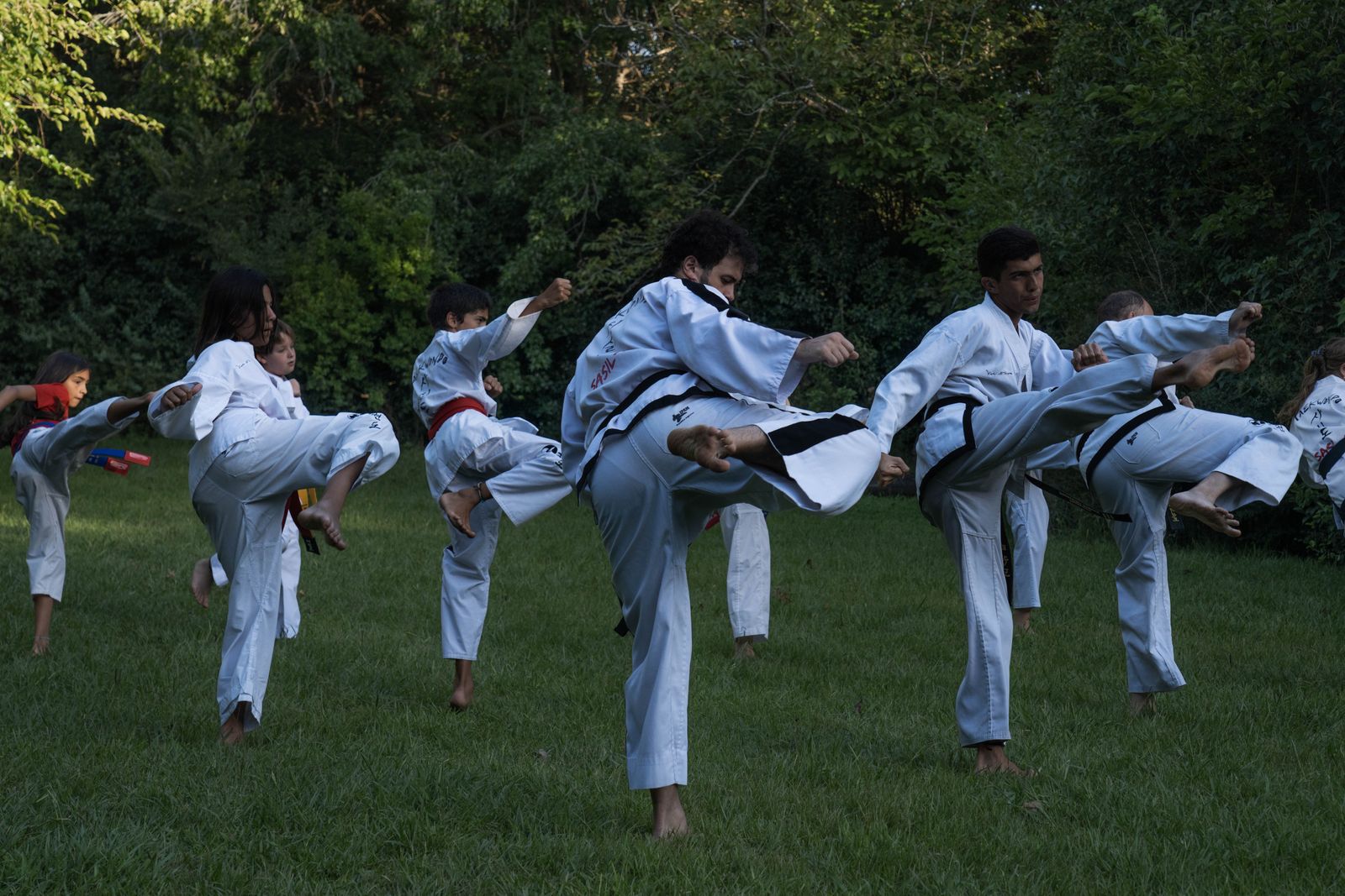 A taekwondo class kicking together outdoors