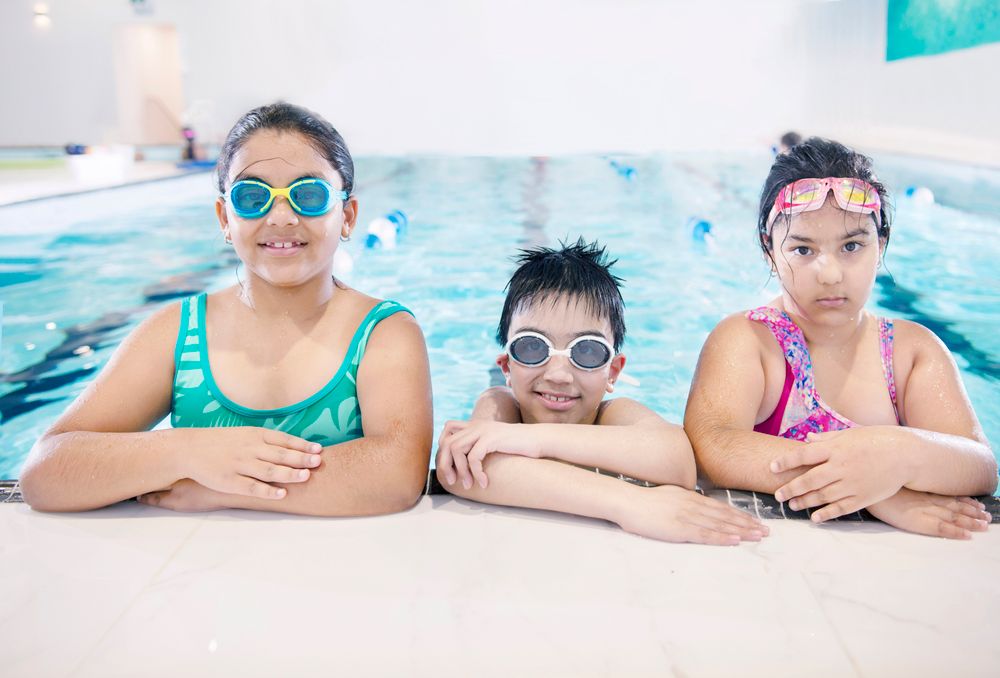 Three children in goggles at the edge of the pool